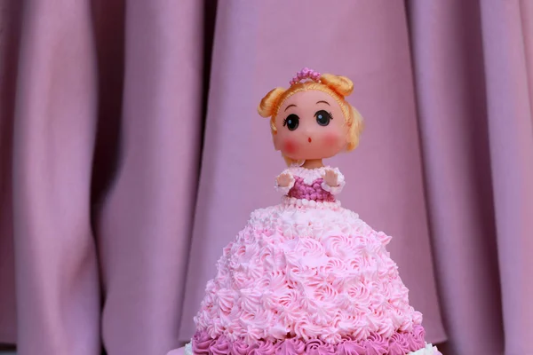 Princess doll cake with dress made of pink cream on pink curtain background.