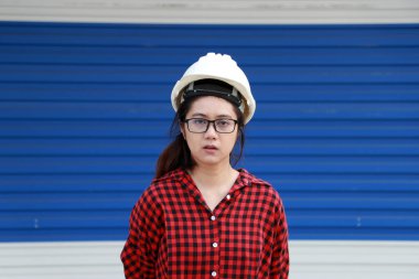 Kadın inşaat mühendisi ya da mimar beyaz kasklı ve mavi arka planda kırmızı ekose elbise giyiyor.. 