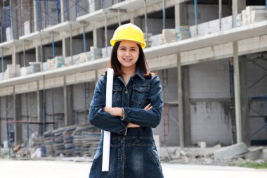 İnşaat mühendisi ya da mimar, sarı kasklı, ayakta duran ve iş yerinde sandık başında taslak çizen kadın..