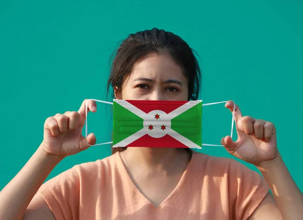一名戴着布隆迪国旗 戴着卫生面具的妇女举着绿色背景的前脸 微小颗粒或病毒电晕或Covid 19保护 防治疾病的概念 — 图库照片