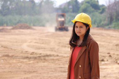 İnşaat mühendisi ya da mimar sarı başlıklı kadın inşaat aracının arka planında duruyor..