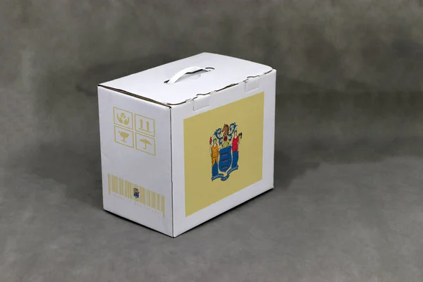 白色盒子上有新泽西州国旗 灰色背景上有脆弱符号的州旗条形码 新泽西出口贸易的概念 产品的纸包装 — 图库照片