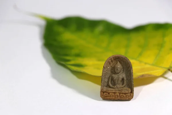 白い床に黄色と緑の神聖なイチジクや菩提樹の葉を持つ小さな仏像のお守り 心臓へのアンカーの使用 — ストック写真