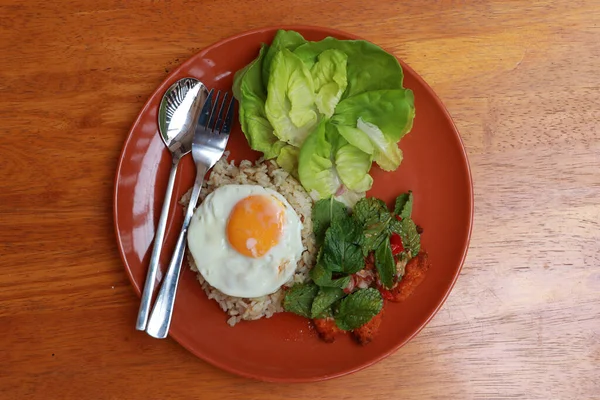 Breakfast in the dark orange color of round plate on the wooden floor. Fried egg brown rice and blend of fried chicken with lettuce vegetable.