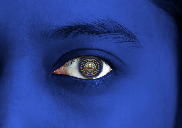 Human face painted New Hampshire flag with the state seal on the center of eye or eyeball. Human eye painted with flag of New Hampshire.