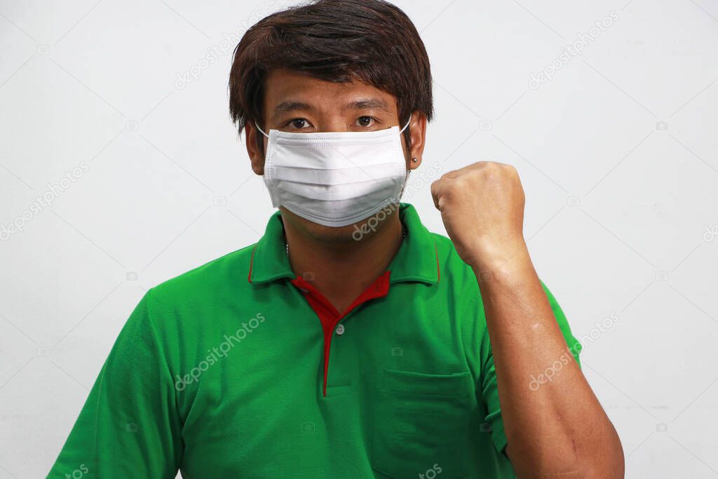 Masked Asian man prevent germs and wear green shirt. Tiny Particle or virus corona or Covid 19 protection. Lift the fist up for meaning fighting or concept of Combating illness.