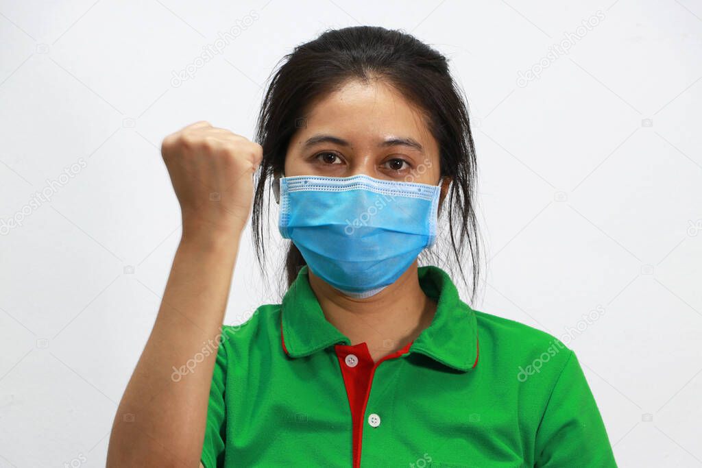 Masked Asian woman prevent germs and wear green shirt. Tiny Particle or virus corona or Covid 19 protection. Lift the fist up for meaning fighting or concept of Combating illness.