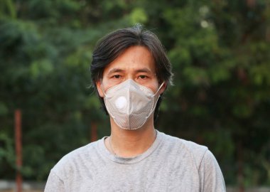 Maskeli Asyalı adam mikropları önler ve gri gömlek giyer. Minik parçacık ya da virüs koronası ya da Covid 19 koruması. Hastalıkla mücadele kavramı.