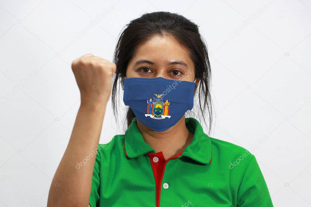 New York flag on hygienic mask. Masked woman prevent germs and wear green shirt. Tiny Particle or virus corona or Covid-19 protection. Lift the fist up for meaning fighting or concept of Combating illness.