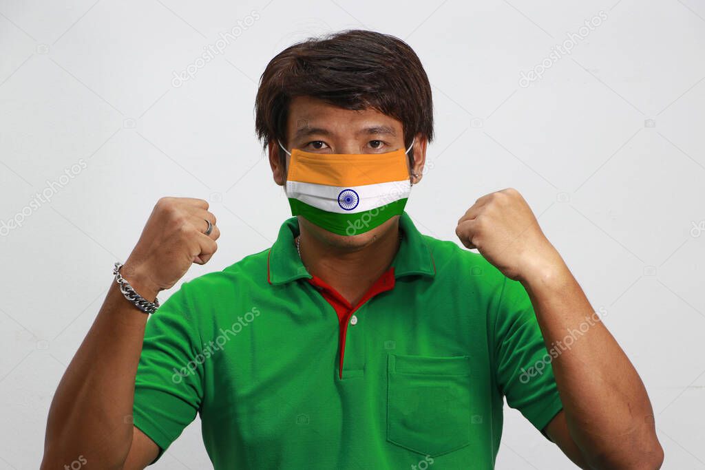 India flag on hygienic mask. Masked Asian man prevent germs and wear orange shirt. Tiny Particle or virus corona or Covid-19 protection. Lift the fist up for meaning fighting or concept of Combating illness.