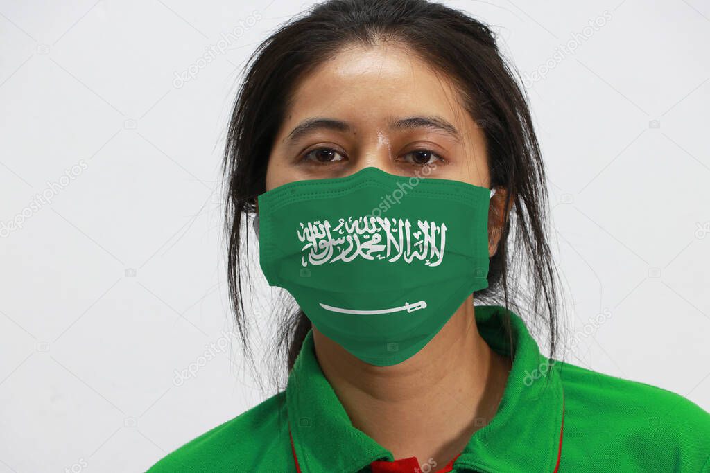 Saudi Arabia flag on hygienic mask. Masked woman prevent germs and wear green shirt. Tiny Particle or virus corona or Covid-19 protection. Arabic word 