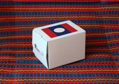 Çizgili arka planı olan beyaz kutuda Lao bayrağı, koyulan ürünler için kağıt ambalaj. Laos 'tan ihracat ticareti kavramı.