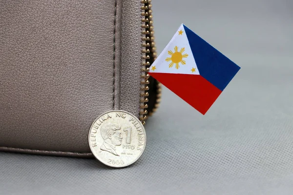 グレーの背景にある革の財布には 海外とミニフィリピンの旗の上にフィリピンペソのお金の1コインが付着しています 通貨の概念 — ストック写真