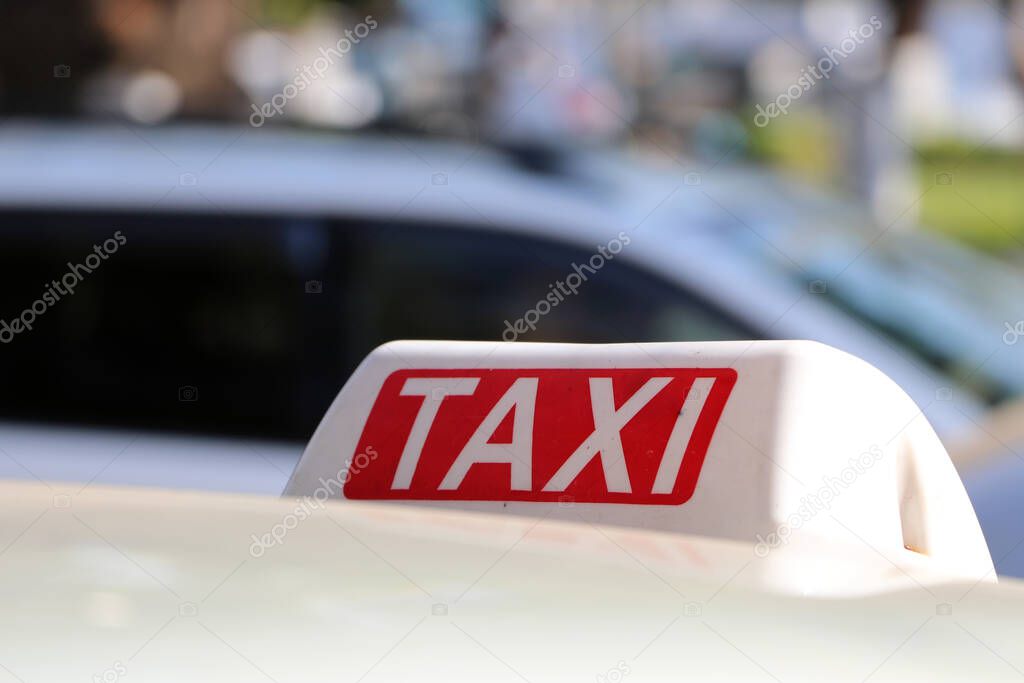 Taxi light sign or cab sign in white and red color with white text on the car roof at the street blurred background, Myanmar.