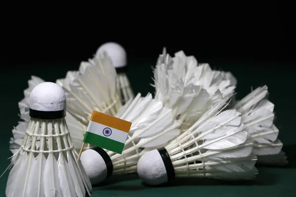 Mini India flag stick on the heap of used shuttlecocks on green floor of Badminton court with dark black background.