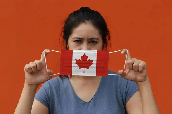 一位手里拿着加拿大国旗 戴着卫生面具的妇女 用橙色的背景把脸抬起来 微小颗粒或病毒电晕或Covid 19保护 防治疾病的概念 — 图库照片