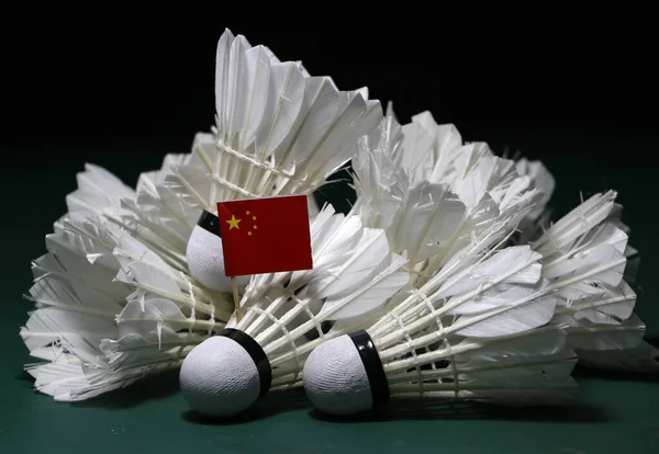 Mini China flag stick on the heap of used shuttlecocks on green floor of Badminton court with dark black background.
