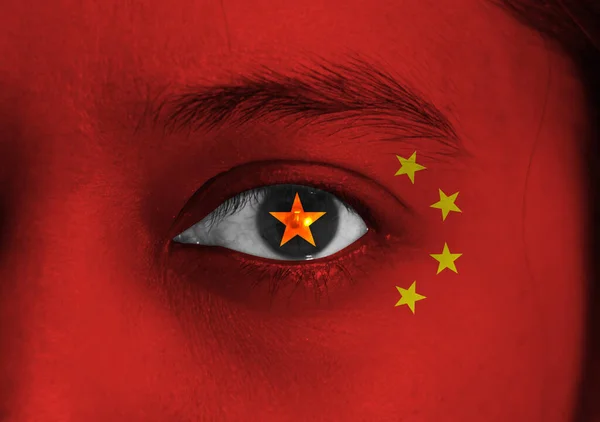 Human face painted China flag with yellow star on the center of eye or eyeball. Human eye painted with flag of China.