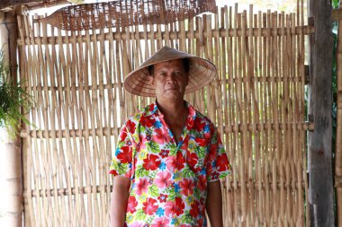 Vietnam konik şapkası takan, çiçekli gömlekli bambu kafes duvarlı arka planda duran adam..