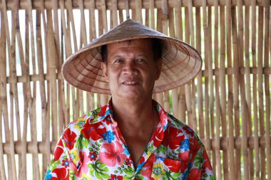 Vietnam konik şapkası takan, çiçekli gömlekli bambu kafes duvarlı arka planda duran adam..