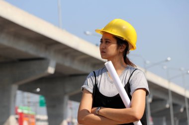 İnşaat mühendisi ya da mimar, sarı kasklı, ayakta duran ve iş yerinde sandık başında taslak çizen kadın..