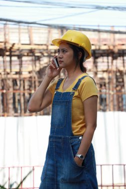 İnşaat mühendisi ya da mimar, sarı kasklı, ayakta ve cep telefonuyla arıyor..