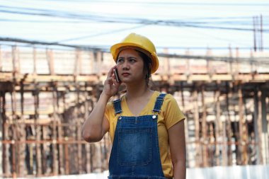 İnşaat mühendisi ya da mimar, sarı kasklı, ayakta ve cep telefonuyla arıyor..