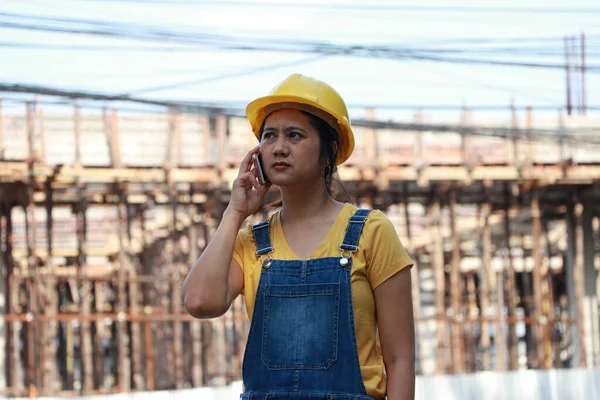 İnşaat mühendisi ya da mimar, sarı kasklı, ayakta ve cep telefonuyla arıyor..