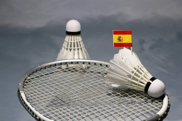 在羽毛球拍网上的羽毛球杆上挂上西班牙国旗 然后把羽毛球杆放在灰色的地板上 — 图库照片