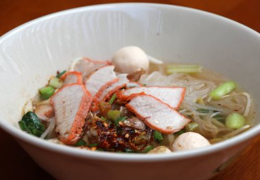 Pirinç çubuklu şehriye çorbası, ahşap masadaki kasede kırmızı domuz rostosu..