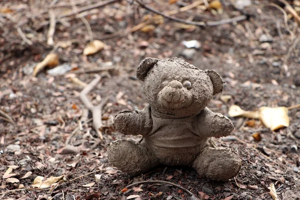 Old dirty teddy bear neglected on the ground soil. End of childhood.