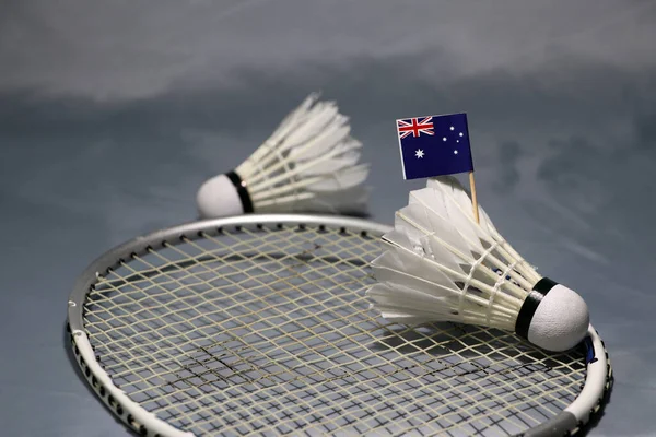 Mini Australia flag stick on the shuttlecock put on the net of badminton racket and out focus a shuttlecock on the grey floor.