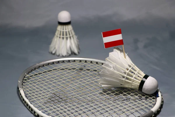 Mini Austria flag stick on the shuttlecock put on the net of badminton racket and out focus a shuttlecock on the grey floor.