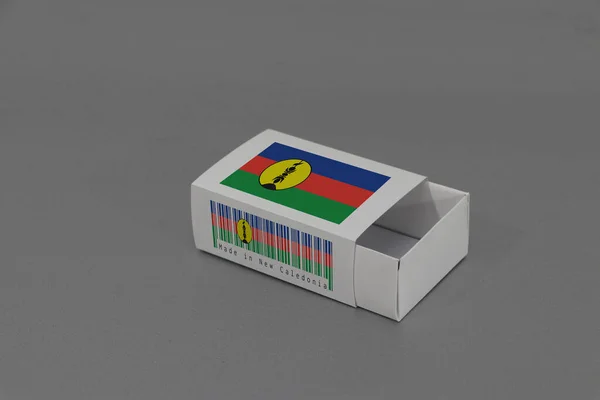 新喀里多尼亚的国旗挂在白色的盒子上 上面有条形码和灰色背景的国旗的颜色 纸包装用于搭配或产品 新喀里多尼亚出口贸易的概念 — 图库照片