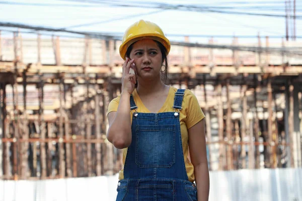 带着黄色头盔的女土木工程师或建筑师 在工作区用手机站立和呼叫 — 图库照片