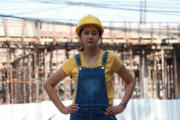 İnşaat mühendisi ya da mimar sarı kasklı, ayakta duran ve çalışma alanında akimbo yapan bir kadın..