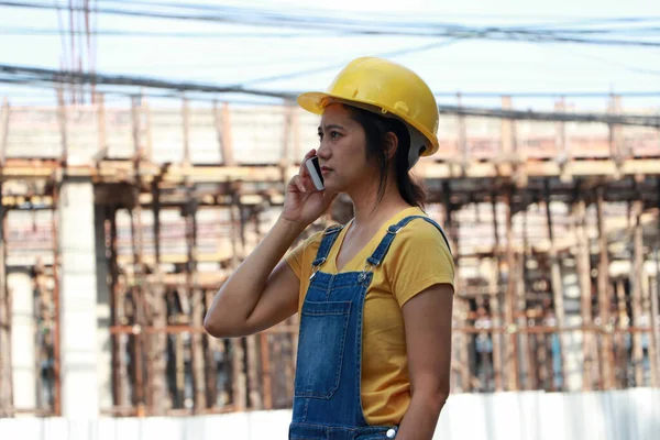 İnşaat mühendisi ya da mimar, sarı kasklı, ayakta ve cep telefonuyla arıyor..