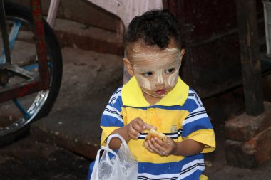 Yangon, Myanmar, 24 Şubat 2019: Yüzünde thanakha olan Myanmalı çocuk, lezzetli bir şekilde tatlı yiyor..