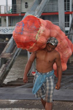 Yangon, Myanmar, 24 Şubat 2019: Myanmese işçisi gemiden hindistan cevizi kabuğu taşıyor ve Yangon Nehri 'ndeki liman köprüsünü geçiyor.