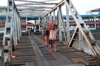 Yangon, Myanmar, 24 Şubat 2019: İki Myanmalı işçi gemiden ördek yumurtaları taşıyor ve Yangon Nehri 'ndeki liman köprüsünü yürüyerek geçiyorlar..