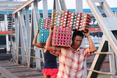 Yangon, Myanmar, 24 Şubat 2019: İki Myanmalı işçi gemiden ördek yumurtaları taşıyor ve Yangon Nehri 'ndeki liman köprüsünü yürüyerek geçiyorlar..