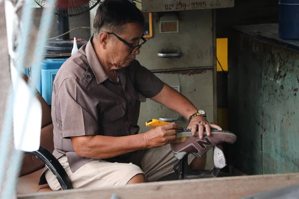 Lat Lum Kaeo, Pathum Thani, Tayland, Sep 9, 2019: Ayakkabı tamirinde uzman olan yaşlı bir adam ayakkabılarını tamir ediyor..