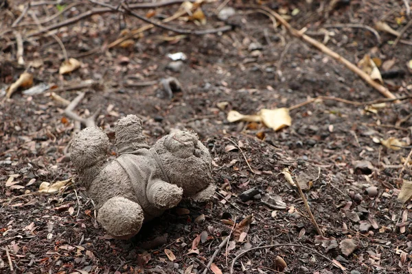 Old dirty teddy bear neglected on the ground soil. End of childhood.