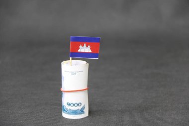 Bin Kamboçya Riel 'ı gibi yuvarlanmış para ve koyu gri zemin ve arka planda mini Kamboçya bayrağı. Finans sektörü kavramı.
