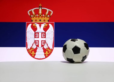 Beyaz zeminde beyaz, mavi ve kırmızı renkli küçük bir futbol topu, Sırp bayrağının arka planında kartal ve taç resmi. Spor konsepti.
