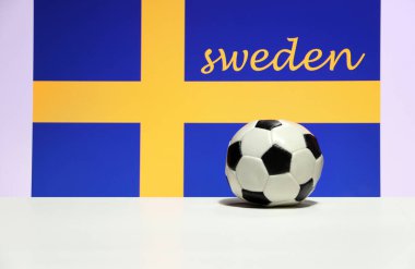 Beyaz zeminde küçük bir futbol topu ve İsveç arka planında İsveç bayrağı. Spor konsepti.