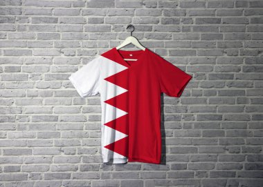 Gömlekte bahreyn bayrağı, duvarda tuğla desenli duvar kâğıdı asılı, kırmızı alanda zigzag şeklinde beş beyaz üçgen..