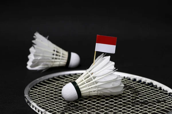 Mini Indonesia flag stick on the shuttlecock put on the net of badminton racket and out focus a shuttlecock on the black floor.