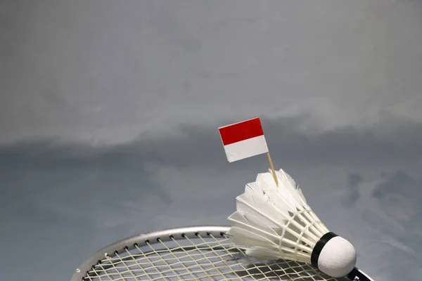 Mini Indonesia flag stick on the shuttlecock put on the net of badminton racket on the grey floor. Concept of badminton sport.