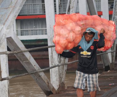 Yangon, Myanmar, 24 Şubat 2019: Myanmese işçisi gemiden hindistan cevizi kabuğu taşıyor ve Yangon Nehri 'ndeki liman köprüsünü geçiyor.